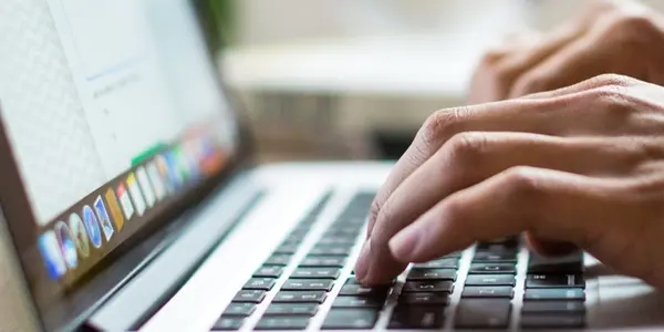 A close up photograph of a pair of hands typing on the keyboard of a laptop computer.