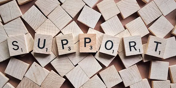 A table top covered in a pile of small blank square wooden tiles. The tiles on top spell out the word SUPPORT.
