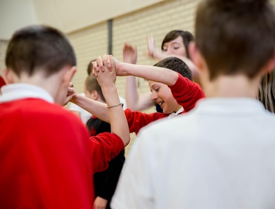 A close up of school children, wearing red and white uniforms, holding hands during ceilidh dancing.