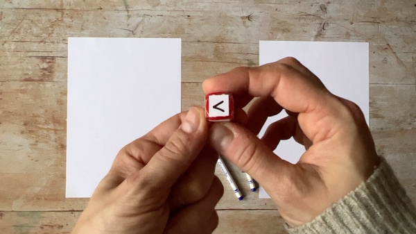 A person holding a dice showing a sideways V sign.