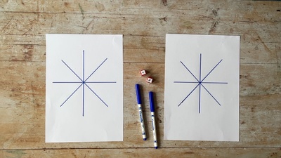 Two sheets of white paper with blue markers and dice. Each sheet has a four crossed lines on it.