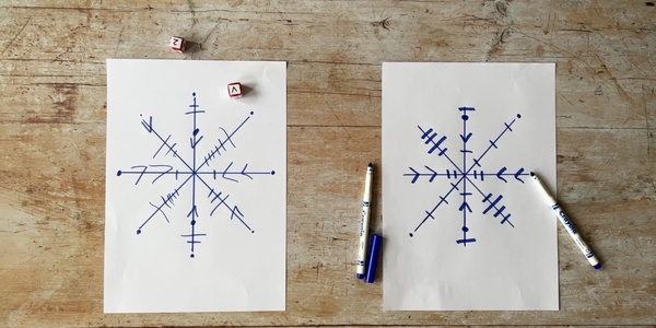 Two sheets of white paper with blue markers and dice. Each sheet has a drawing of a snowflake on it.