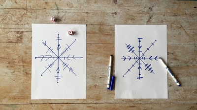 Two sheets of white paper with blue markers and dice. Each sheet has a drawing of a snowflake on it.