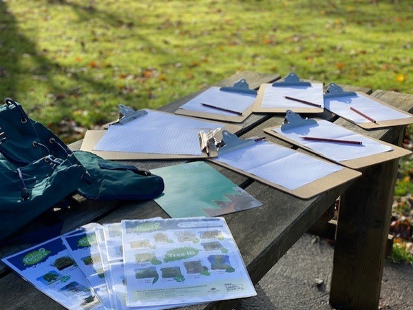 A photograph of a table covered in clipboards and print outs of activity sheets. The table with the clipboard is outdoors.
