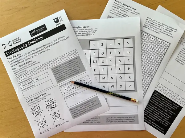 The image shows some printed out pages. Each page has a different cryptography puzzle on it. On top of the pages is a pencil.