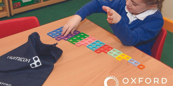 A child is sitting at a table playing with Numicon maths pieces. In front of here is a black Numicon bag.